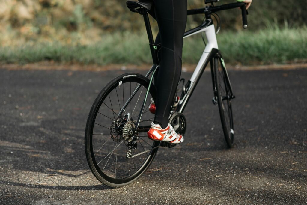 Cyclist with red cleats riding a road bike on an outdoor path.